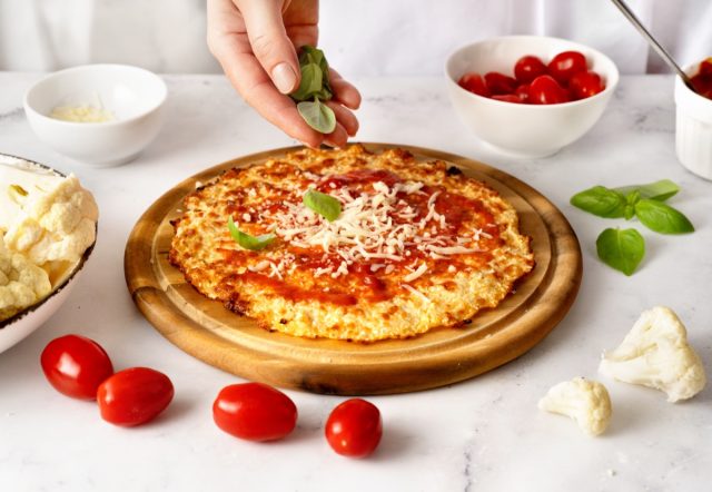 Woman's hands sprinkling fresh basil leaves on the top of cauliflower pizza crust