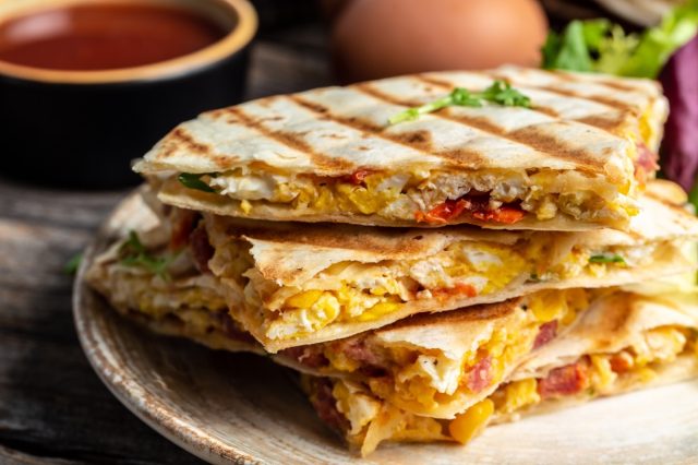 Mexican tortilla quesadilla with scramble eggs, vegetables, ham and cheese, Mexican cuisine, Mexico and Latin America traditional restaurant menu dish, food cooking recipe book cover.