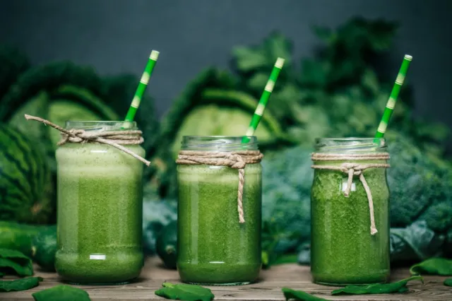 Blended green smoothie with ingredients on wooden table