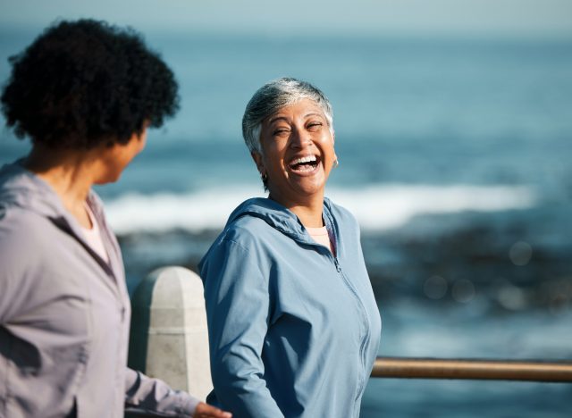 happy mature woman walking on boardwalk by the ocean, concept of tips to live longer