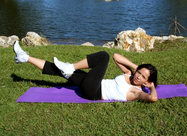 woman doing bicycle crunches on yoga mat outdoors