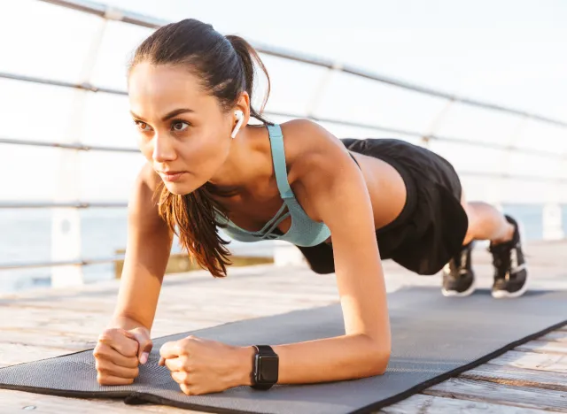 woman doing planks on yoga mat on boardwalk