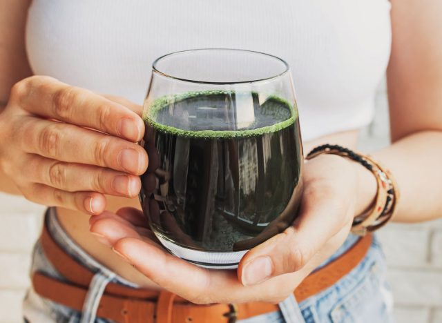 woman holding a glass of greens powder drink