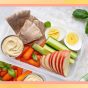 a photo of a high-protein snack plate with apples, carrots, eggs, hummus on a designed background
