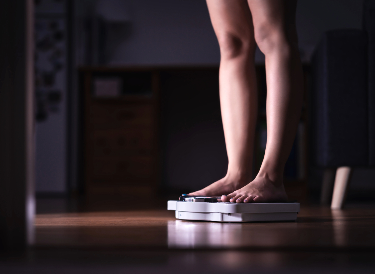 woman weighing herself on scale at night, concept of nighttime habits that cause weight gain