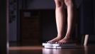 woman weighing herself on scale at night, concept of nighttime habits that cause weight gain