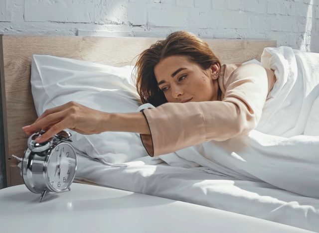 woman turning off alarm in bed