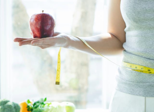 woman holding apple and tape measure, concept of how to lose one pound a week without exercise