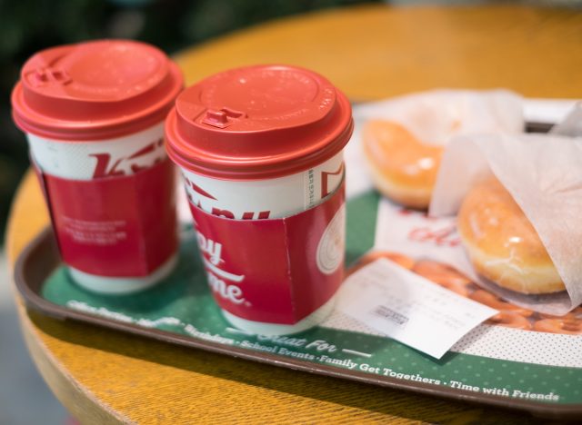 Hot chocolate served in a tall red Christmas cup with krispy kreme donut