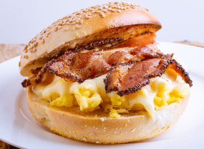 breakfast sandwich of toasted sesame bagel, slab bacon, egg and melted cheese.