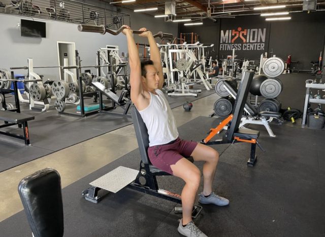 trainer showing how to do EZ bar french press, concept of strength workouts for flabby arms