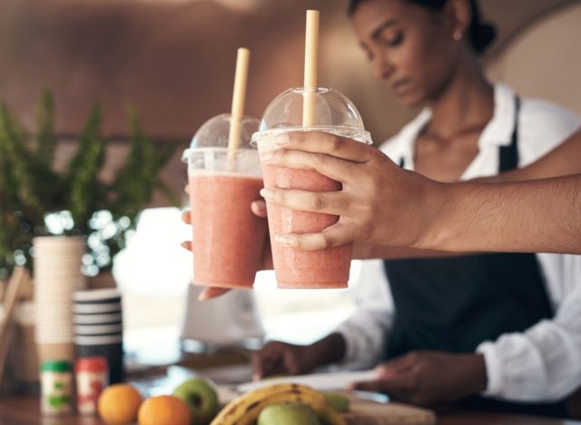 person holding two to-go cups of smoothies