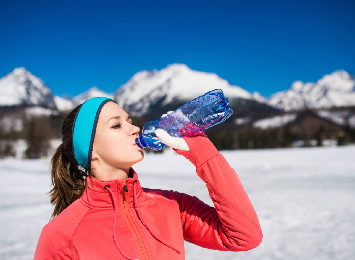 woman drinking water outdoors on snowy day, concept of reasons to drink more water in winter