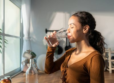 woman drinking water in bright kitchen, concept of how much water to drink for weight loss