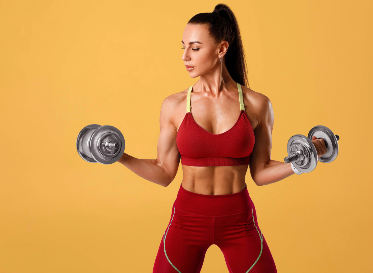 fit woman holding dumbbells in front of yellow background, concept of dumbbell workout for abs in 30 days