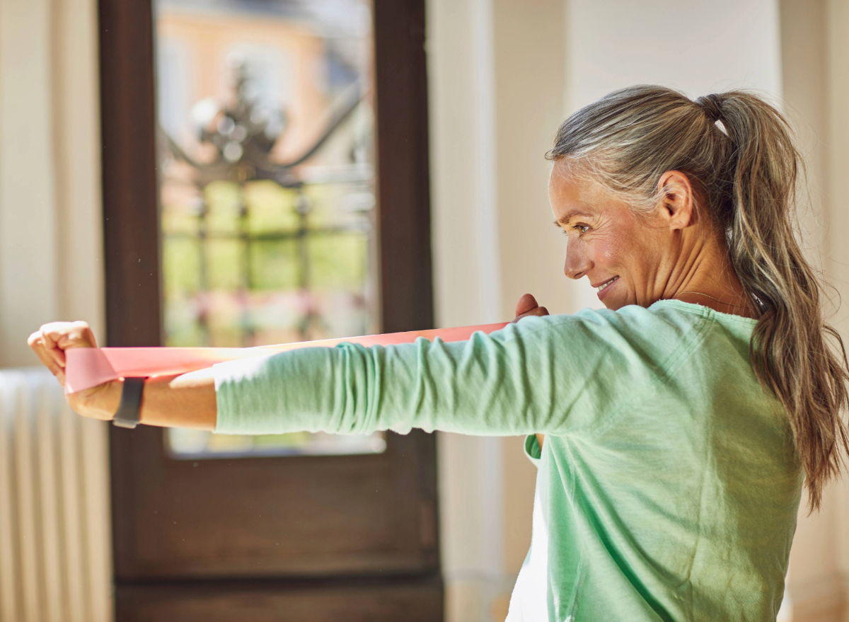 mature woman doing resistance band arm exercise at home, concept of weight-bearing exercises for adults over 50