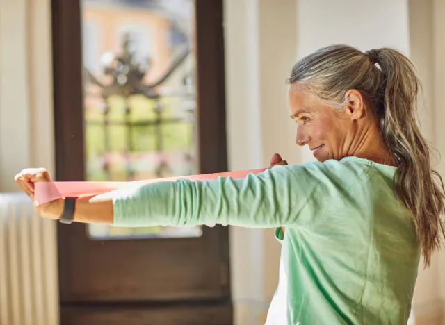 mature woman doing resistance band arm exercise at home, concept of weight-bearing exercises for adults over 50