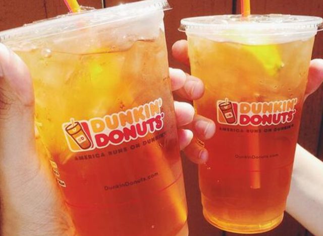 two hands holding two cups of Dunkin' iced teas