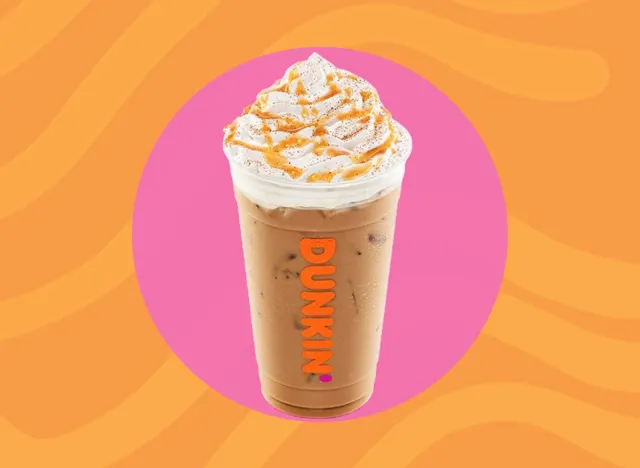 Cup of Dunkin' iced latte with whipped cream on an orange and pink background