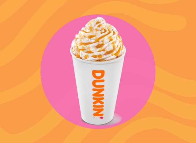 cup of hot Dunkin' drink with whipped cream on a pink and orange background.