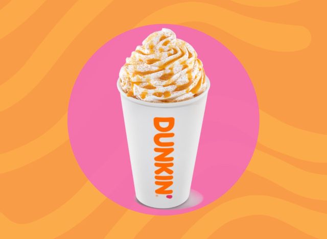 cup of hot Dunkin' drink with whipped cream on a pink and orange background.