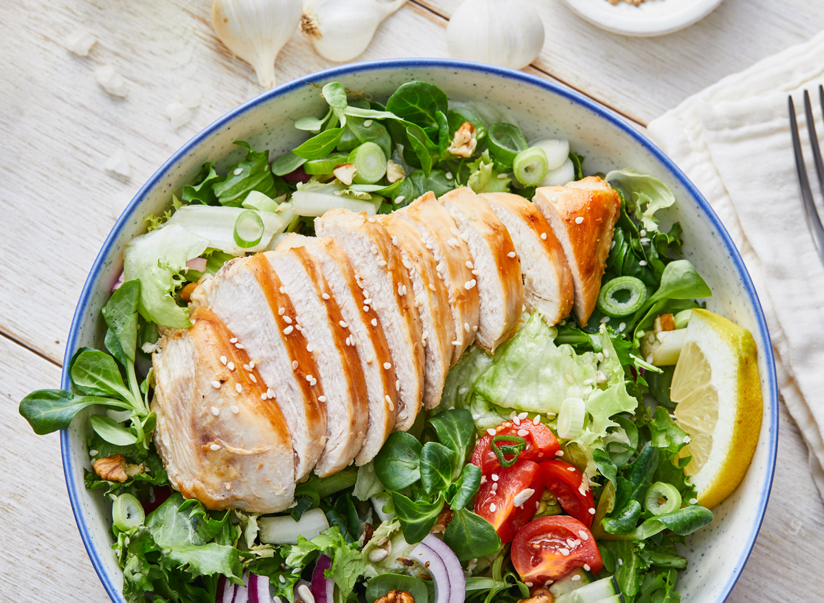 sliced baked chicken on top of a leafy greens salad