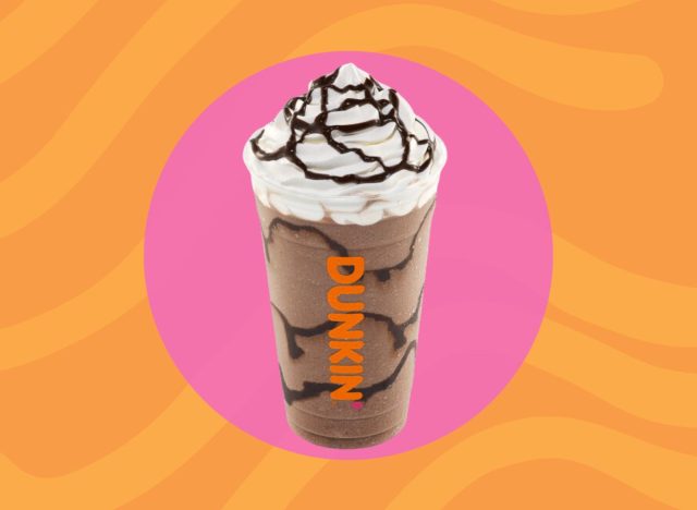 Cup of Dunkin' frozen chocolate drink with whipped cream on a pink and orange background.