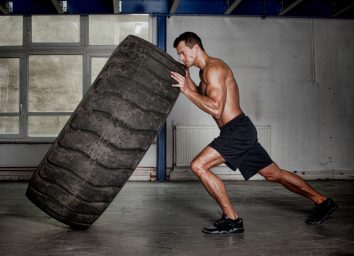 fit man lifting tire for strength, concept of how much to strength train depending on your goals