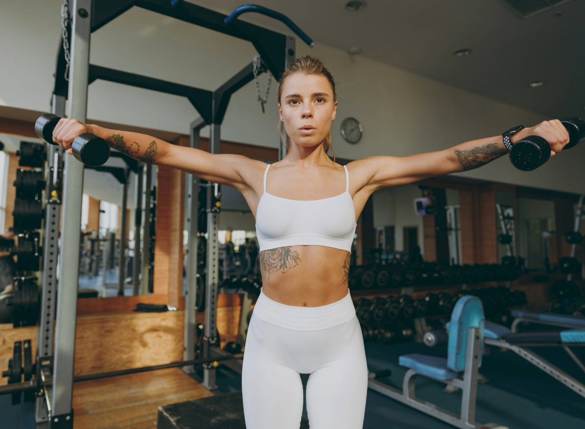 fit woman doing dumbbell raises exercise at the gym, concept of exercises for slimmer arms