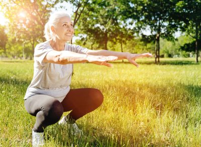 mature woman doing squats outdoors, concept of functional strength exercises for mobility