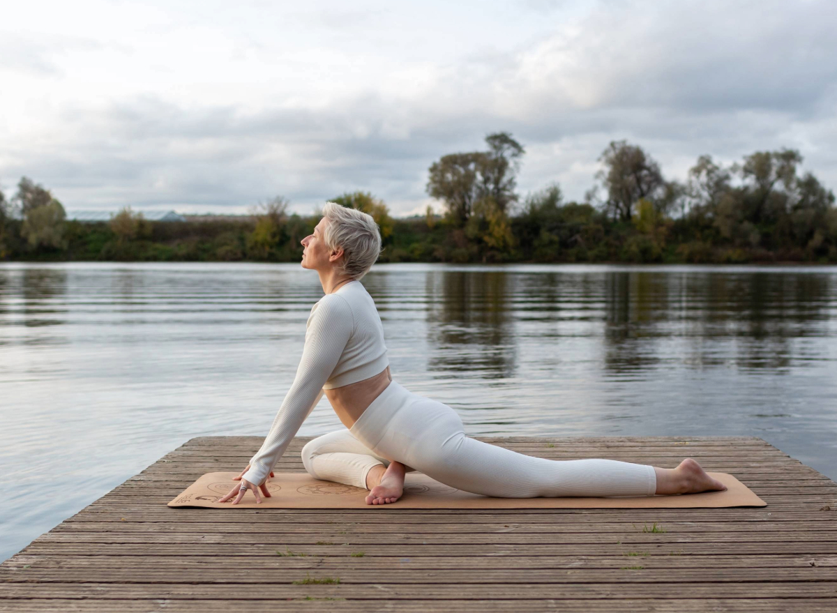mature woman doing pigeon pose on dock by lake, concept of the best flexibility exercises to stay active and mobile