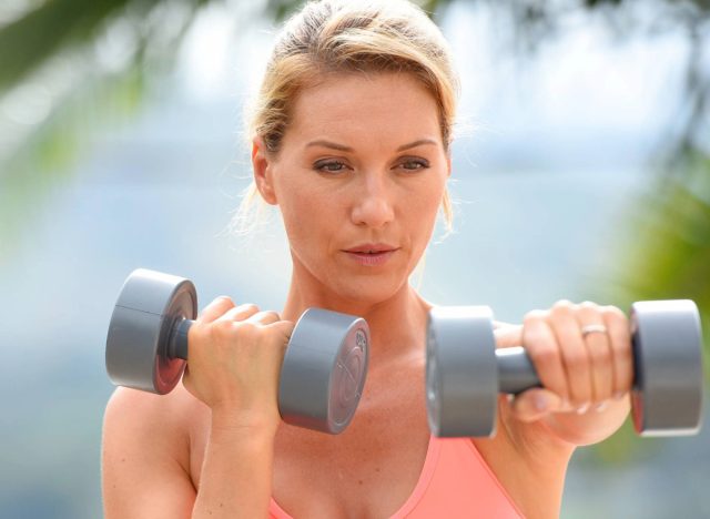 middle-aged woman doing dumbbell exercise outdoors, concept of free weight workouts to regain muscle mass