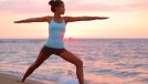 fit woman doing a warrior pose as part of a morning yoga workout on the beach at sunrise