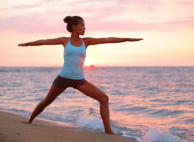 fit woman doing a warrior pose as part of a morning yoga workout on the beach at sunrise