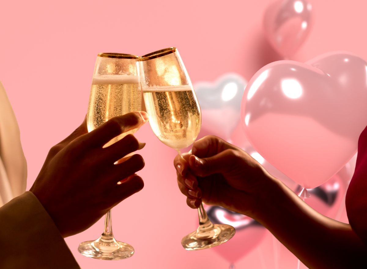 a photo of a couple clinking champagne glasses against a pink background with heart-shaped ballons