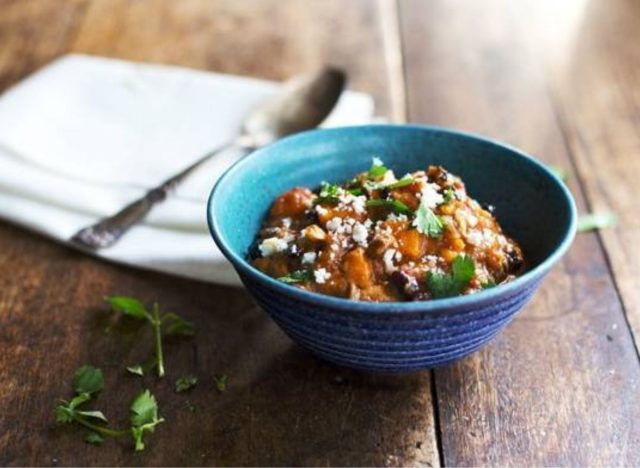 blue bowl of chili with spoon and napkin on a wooden table