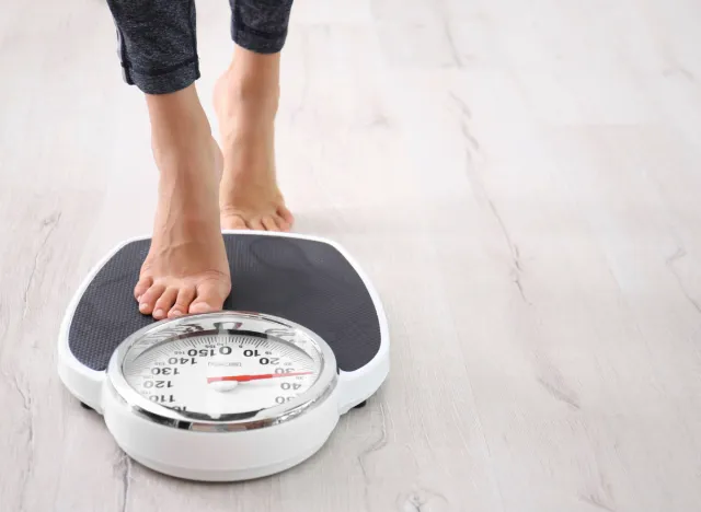 woman stepping on scale, concept of how much weight to safely lose in a month