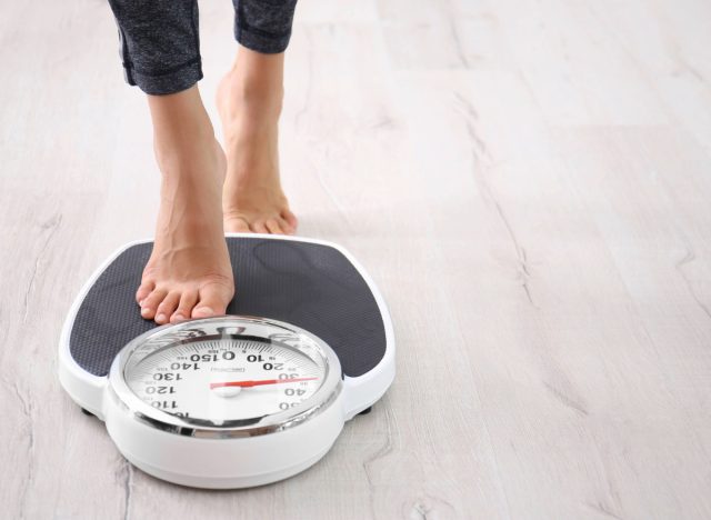 woman stepping on scale, concept of how much weight to safely lose in a month