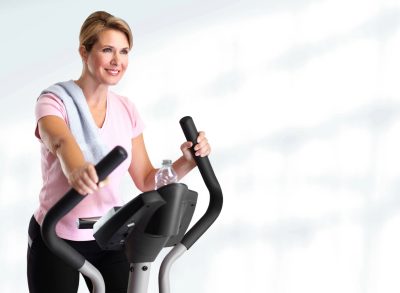 fit middle-aged woman using the elliptical, concept of low-impact cardio exercises for weight loss