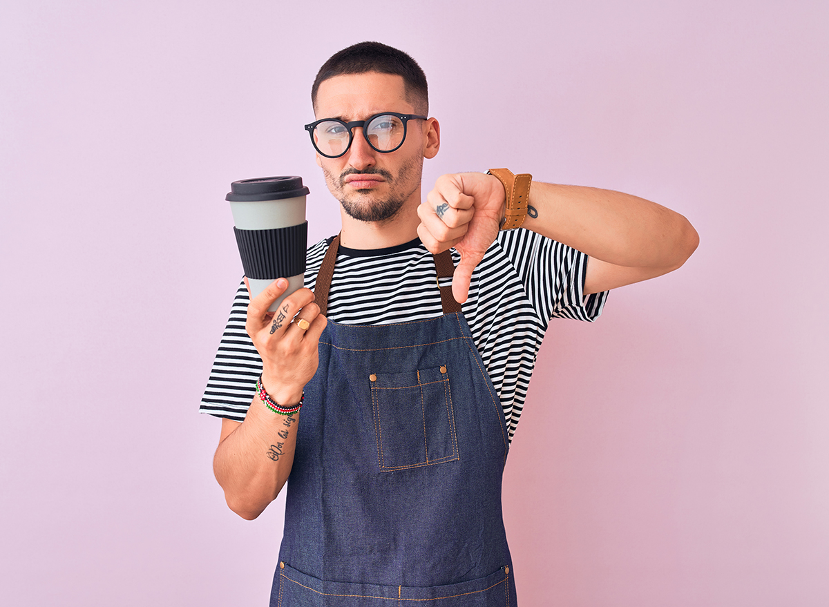 Young barista wearing an apron, showing dislike with thumbs down