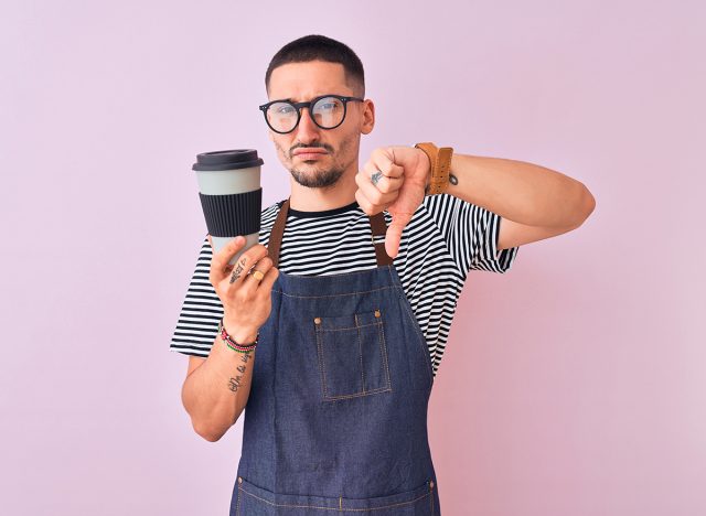 Young barista wearing an apron, showing dislike with thumbs down
