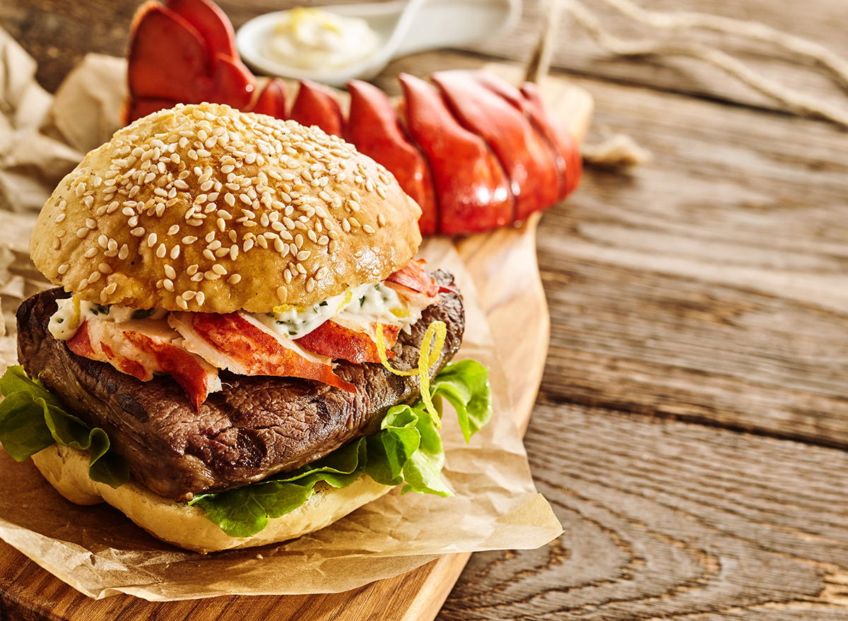 Freshly cooked bacon, lettuce and mayonnaise hamburger with red lobster tail on cutting board
