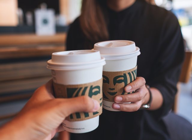 Closeup of a couple people holding and clinking two cup of hot coffee at Starbucks coffee shop