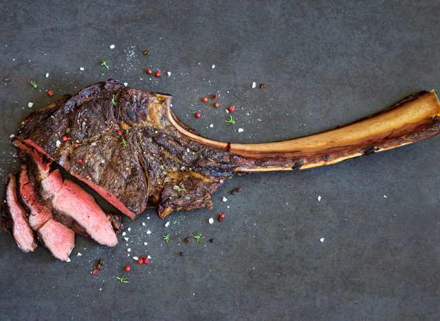 Sliced tomahawk steak with flecks of salt on a gray background