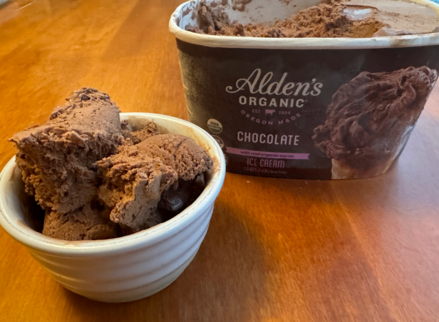 a container of alden's chocolate ice cream open on a table with a bowl of ice cream.