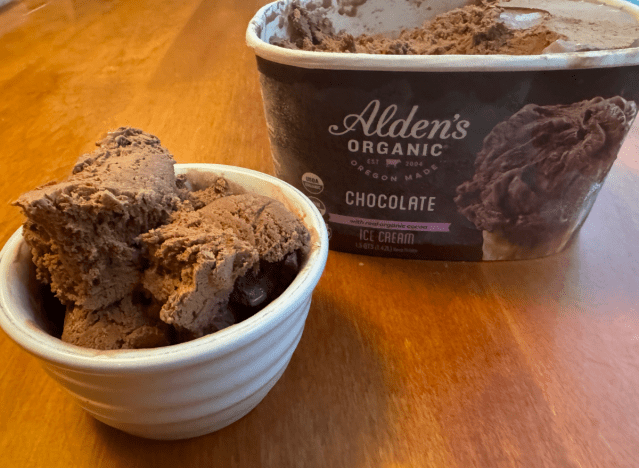 a container of alden's chocolate ice cream open on a table with a bowl of ice cream.