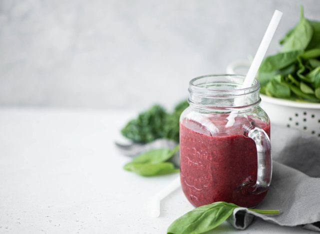berry smoothie in mason jar with white straw next to some spinach