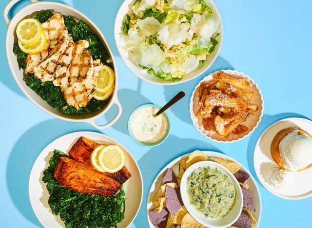 blue background with plates of california pizza kitchen's salmon, chicken, crispy smashed potatoes, Caesar salad, spinach artichoke dip, and classic butter cake with vanilla Häagen-Dazs ice cream
