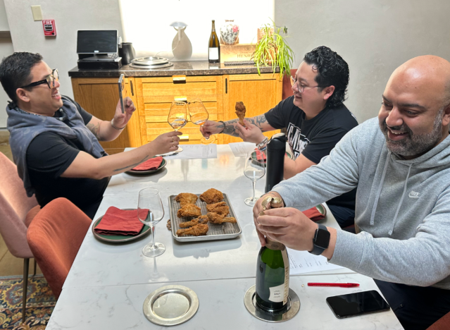 three chefs eating fried chicken at a table.