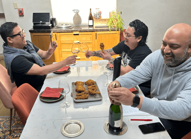 three chefs eating fried chicken at a table.